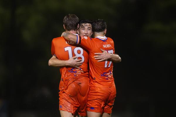 Lions FC players in orange kits embrace in celebration during a match